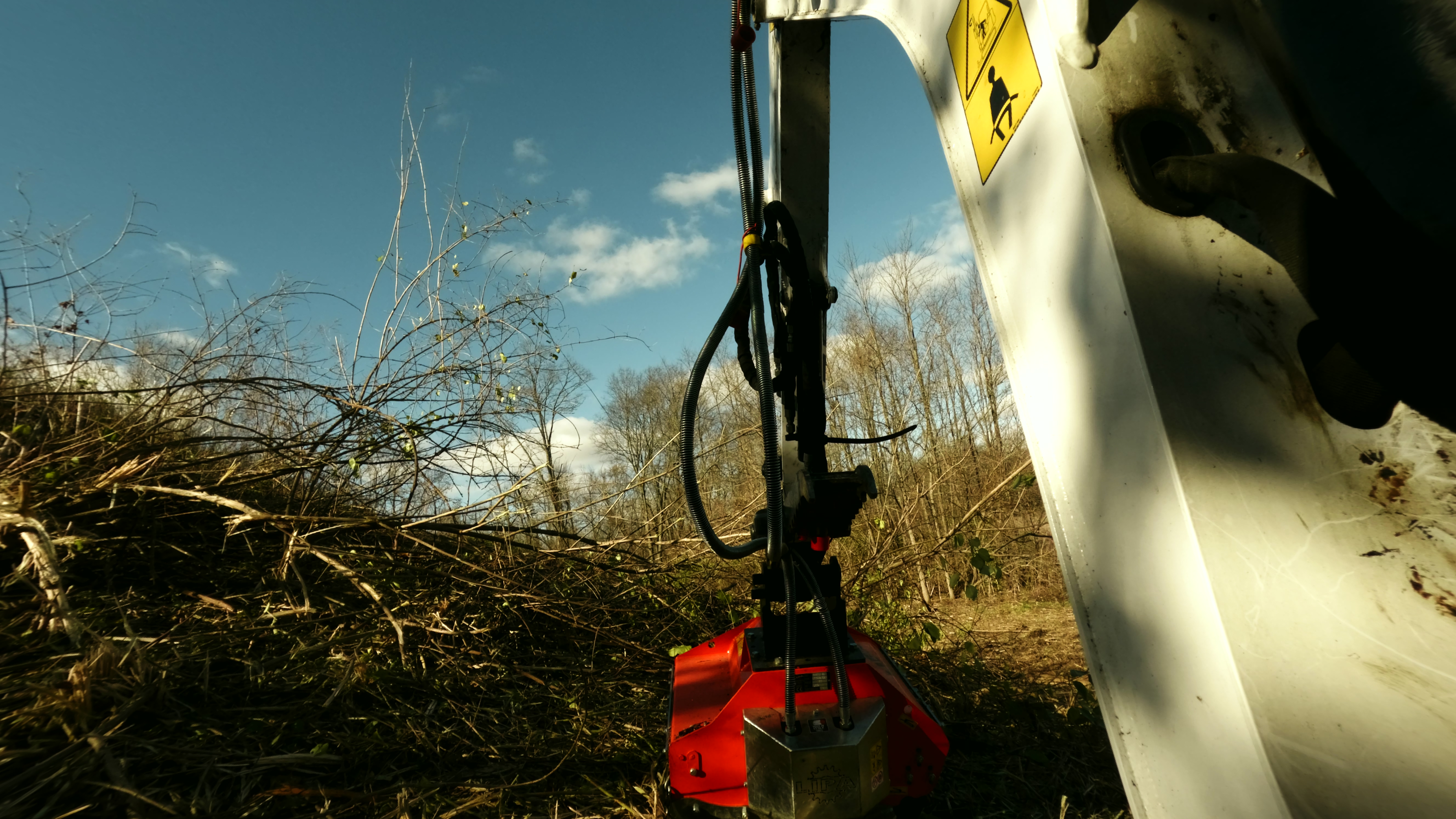 Flail mower clearing brush against sky
